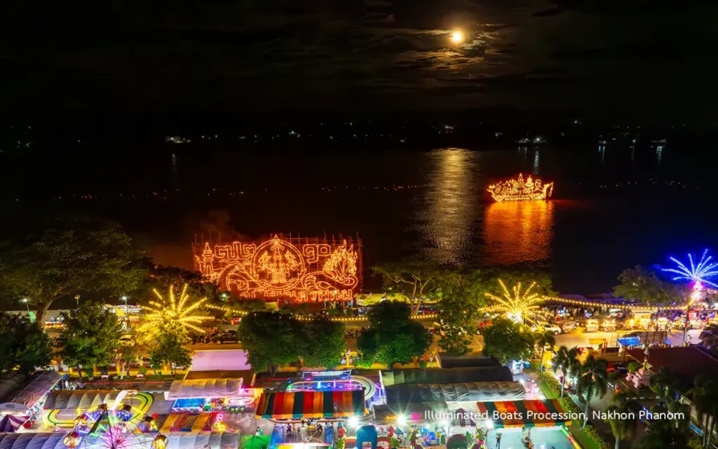 Panoramisch nachtzicht op het Lai Reua Fai-festival, met verlichte boten op de Mekong, kleurrijke attracties en kraampjes langs de rivieroevers van Nakhon Phanom.