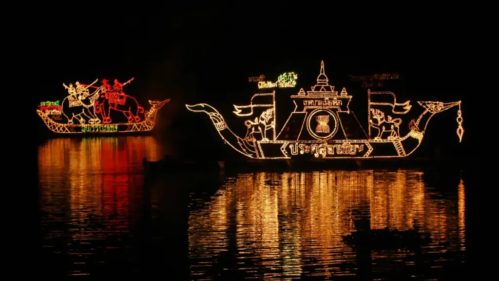 Boten versierd met gouden en rode lichtfiguren op de Mekong tijdens Lai Reua Fai, met kleurrijke weerspiegelingen in het donkere water.