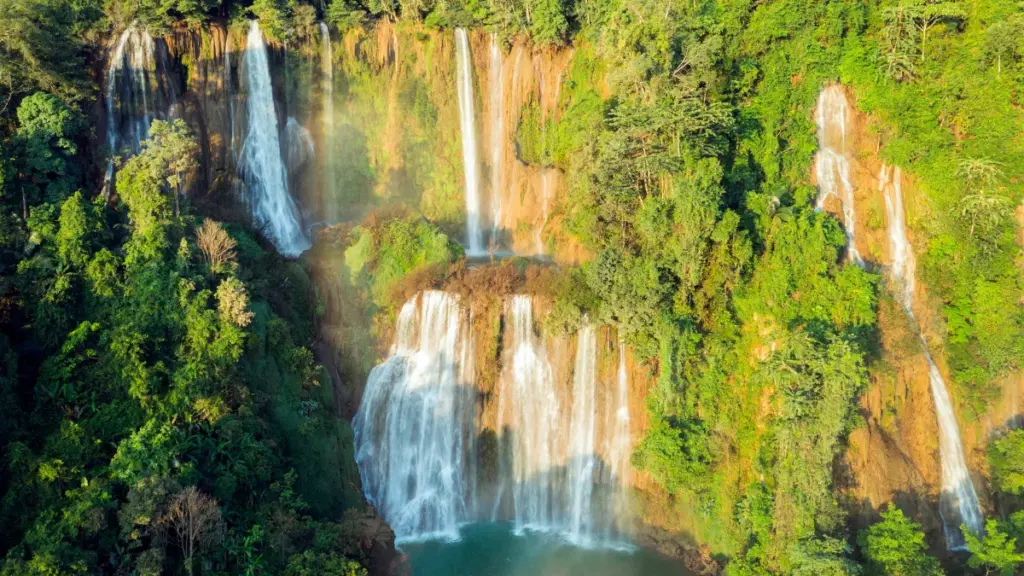 De Thi Lo Su-waterval stroomt in meerdere trappen naar een lichtblauw bassin, tussen bomen en dichte begroeiing.