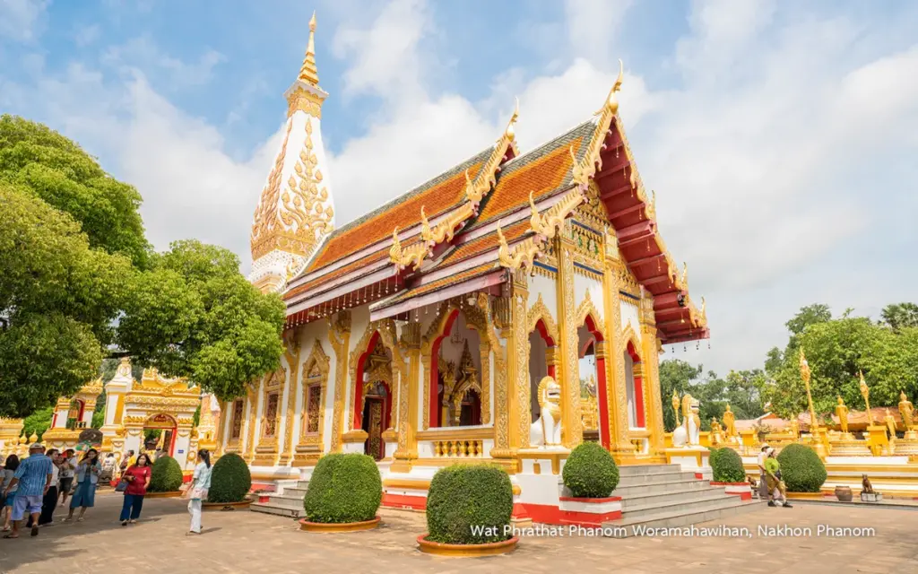 Boeddhistisch tempelgebouw van Wat Phra That Phanom in Nakhon Phanom, met een rood-gouden dak, traditionele beeldhouwwerken, sierlijke zuilen en een grote witte stoepa op de achtergrond.