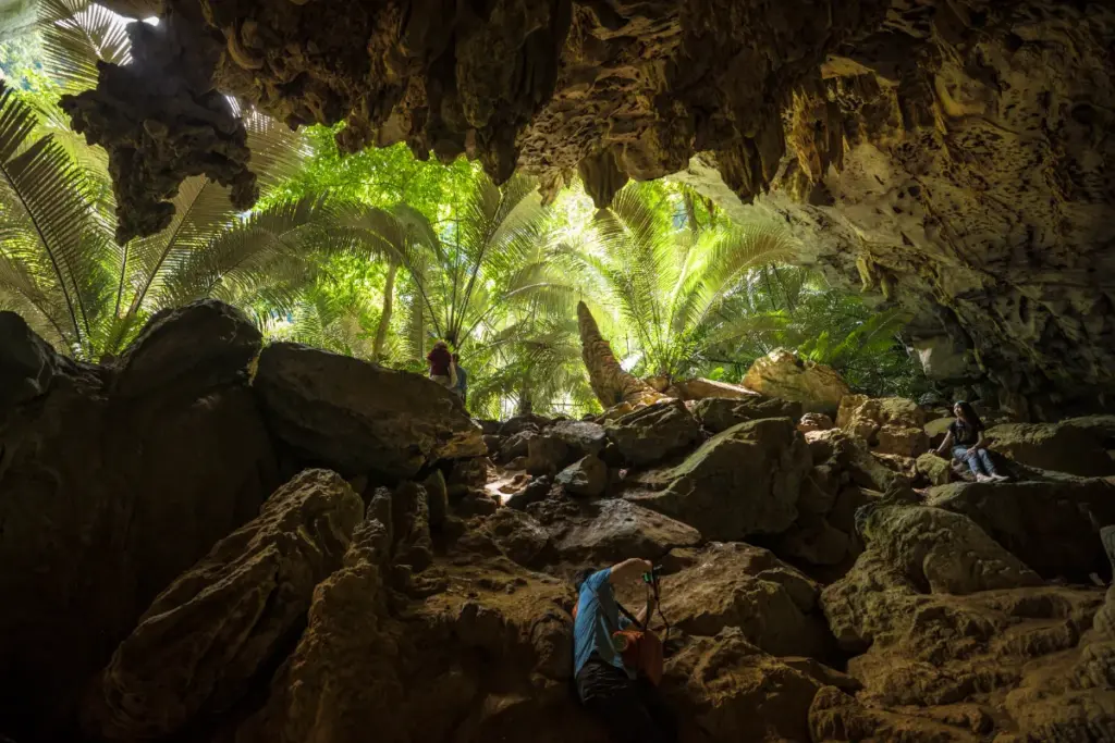 Vue depuis une grotte rocheuse de Hup Pa Tat, avec des palmiers éclairés et plusieurs visiteurs parmi les rochers.