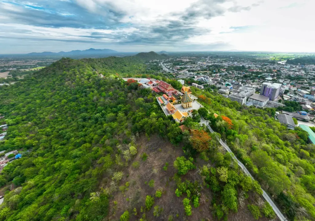 Vue aérienne oblique d'une pagode dorée sur la colline de Khao Sakae Krang, avec la ville en arrière-plan.