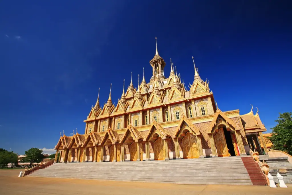 Façade richement décorée d'un bâtiment du Wat Tha Sung, avec ses toits pointus, ses ornements dorés et son grand escalier.