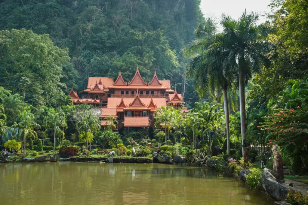 Temple traditionnel en bois de Wat Tham Khao Wong entouré de palmiers, avec un grand étang au premier plan.